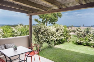 Un patio cubierto con una mesa y sillas, vistas a un jardín ajardinado con arbustos florecientes y un paisaje distante.