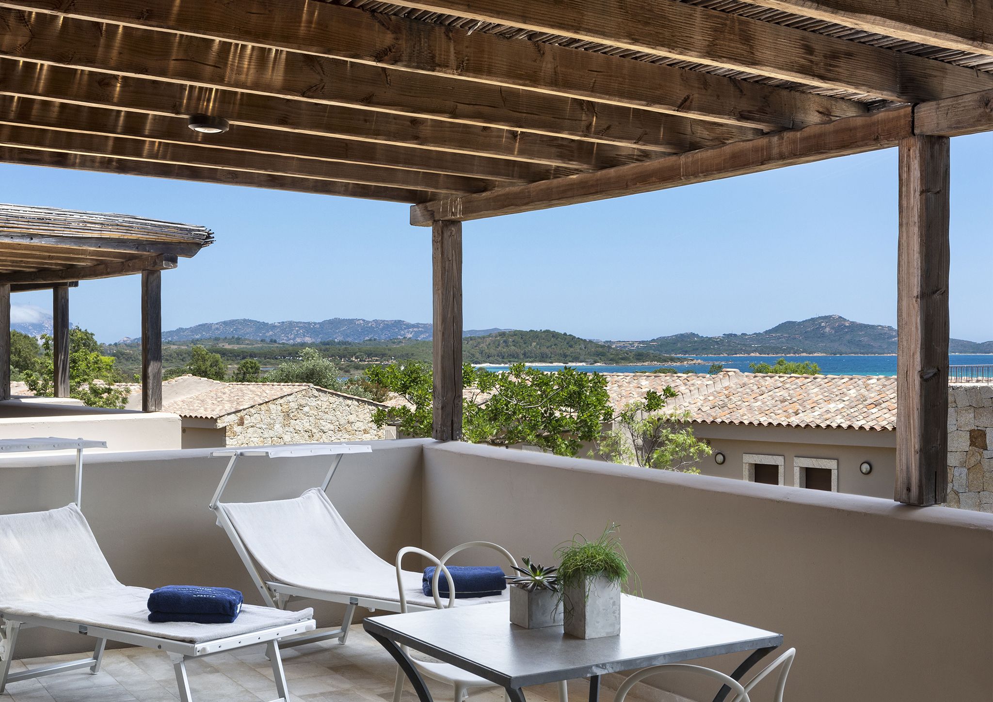 A balcony with two white lounge chairs, a small table, and a potted plant.