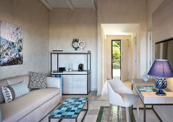 A modern living room with a sofa, coffee table, and a dining area with a lamp. - Baglioni Resort Sardinia (San Teodoro)
