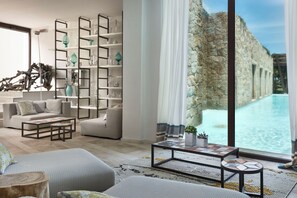 Una sala de estar moderna con un gran ventanal con vistas a una piscina, una estantería empotrada y un rincón de estar acogedor.