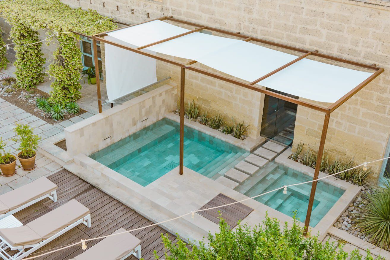 Une piscine sur le toit, protégée par une structure en verre, entourée de chaises longues et de plantes en pot.