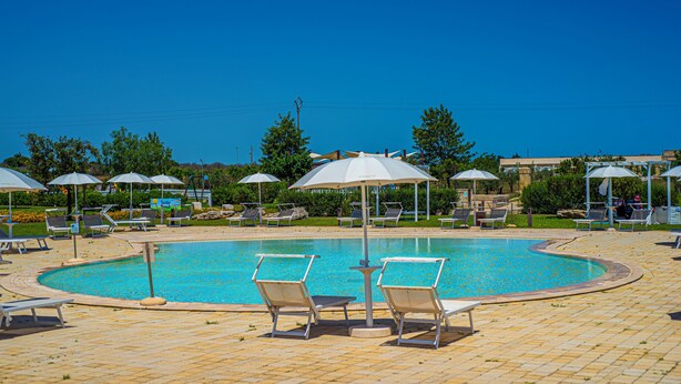 A swimming pool with lounge chairs and umbrellas, surrounded by greenery and a clear sky. - Relais Masseria Le Cesine Cdshotels (Vernole)