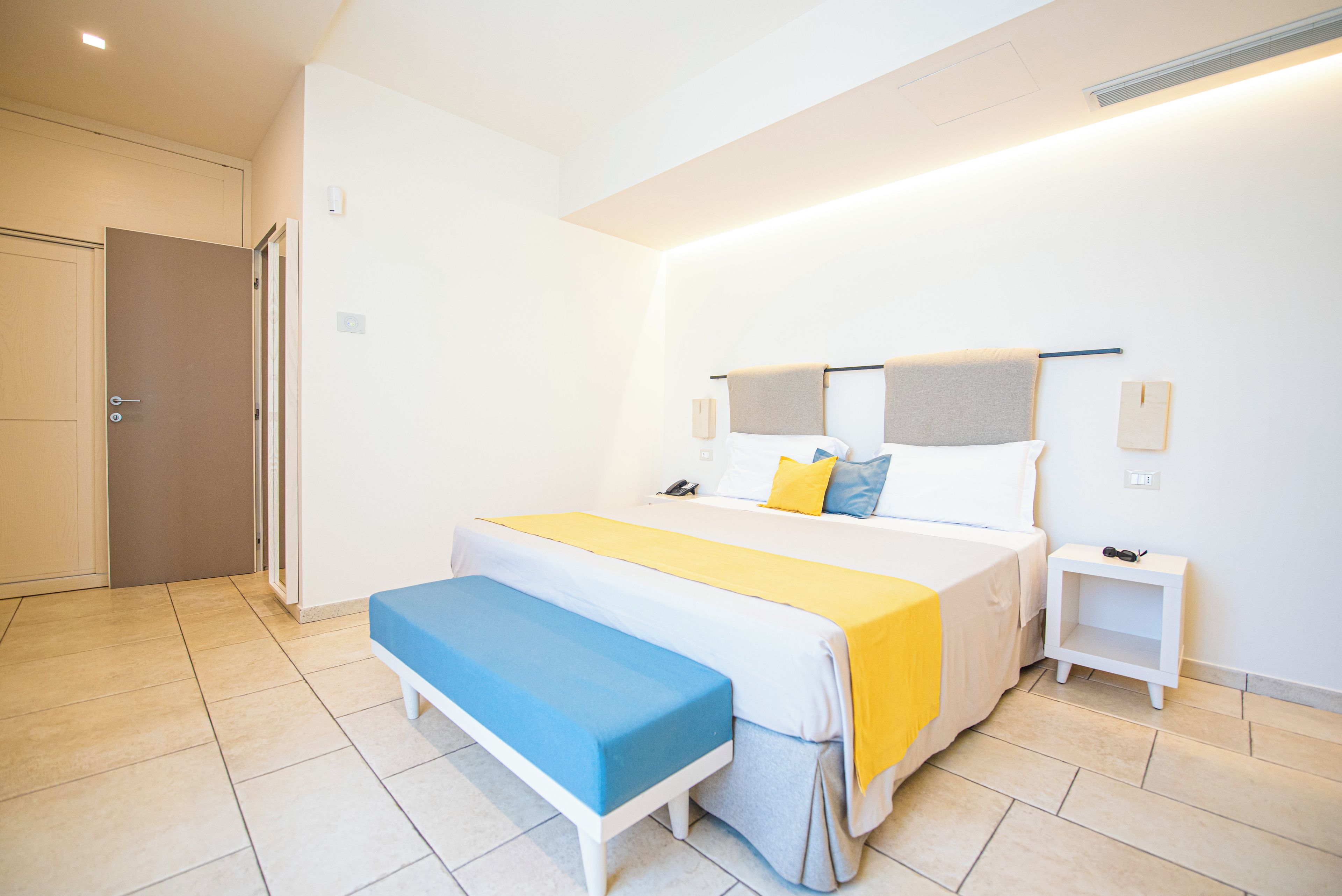 Une chambre à coucher avec un lit, des tables de chevet, un banc et une porte.