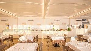 A spacious restaurant with multiple tables and chairs, a central counter with a display of food items, and a modern ceiling design. - Relais Masseria Le Cesine Cdshotels (Vernole)