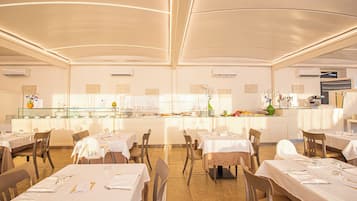 A spacious restaurant with multiple tables and chairs, a central counter with a display of food items, and a modern ceiling design.