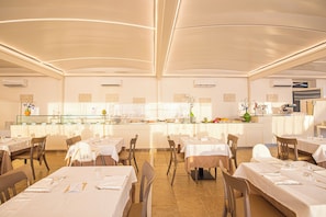 Un restaurante espacioso con varias mesas y sillas, una barra central que exhibe diferentes alimentos, y un diseño de techo moderno.