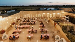Un área de comedor al aire libre con varias mesas y sillas, rodeada de muros de piedra y luces colgantes.