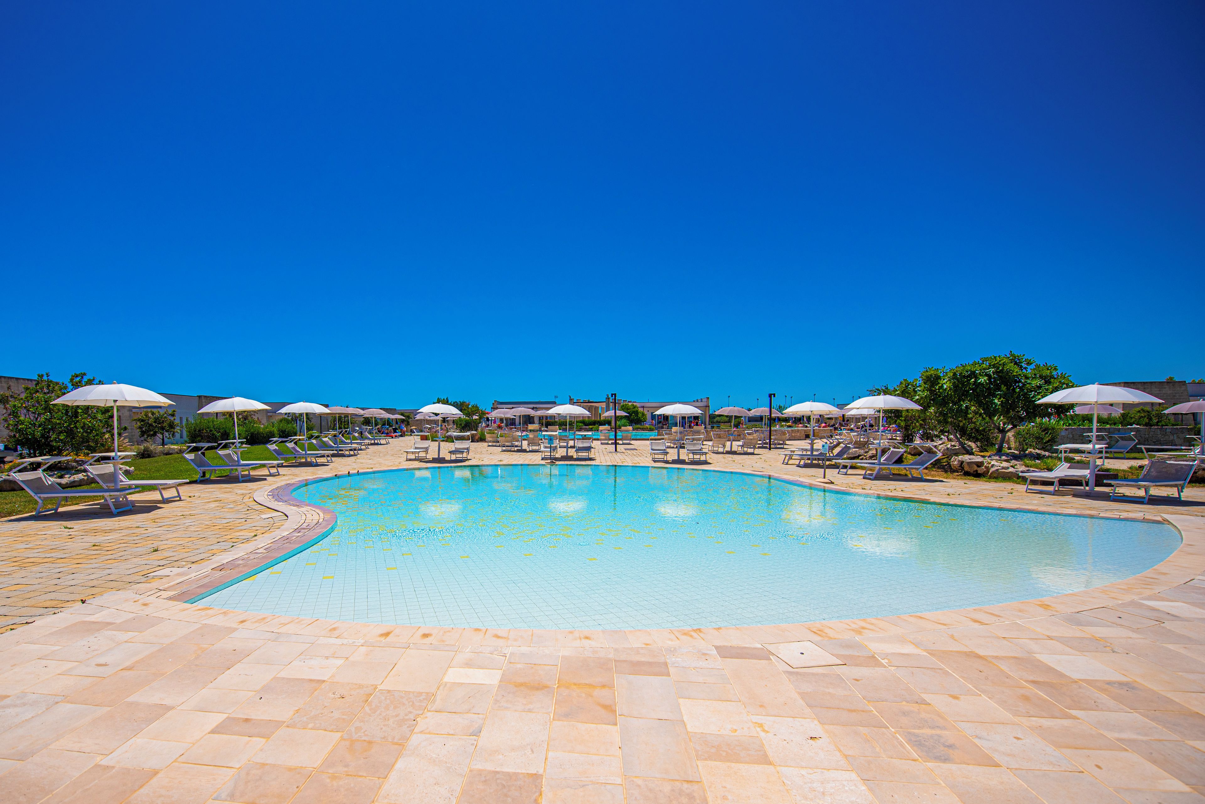 Une grande piscine extérieure, dotée de chaises longues et de parasols, et entourée d’une terrasse carrelée.