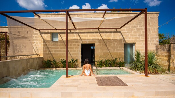 Una mujer sentada junto a una piscina con una estructura de pérgola.