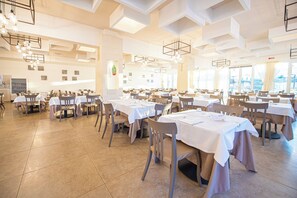 Un comedor amplio con varias mesas y sillas, techos altos decorados con patrones geométricos, y grandes ventanales que permiten la entrada de luz natural.