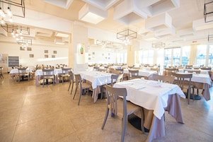 Un comedor amplio con varias mesas y sillas, techos altos decorados con patrones geométricos, y grandes ventanales que permiten la entrada de luz natural.