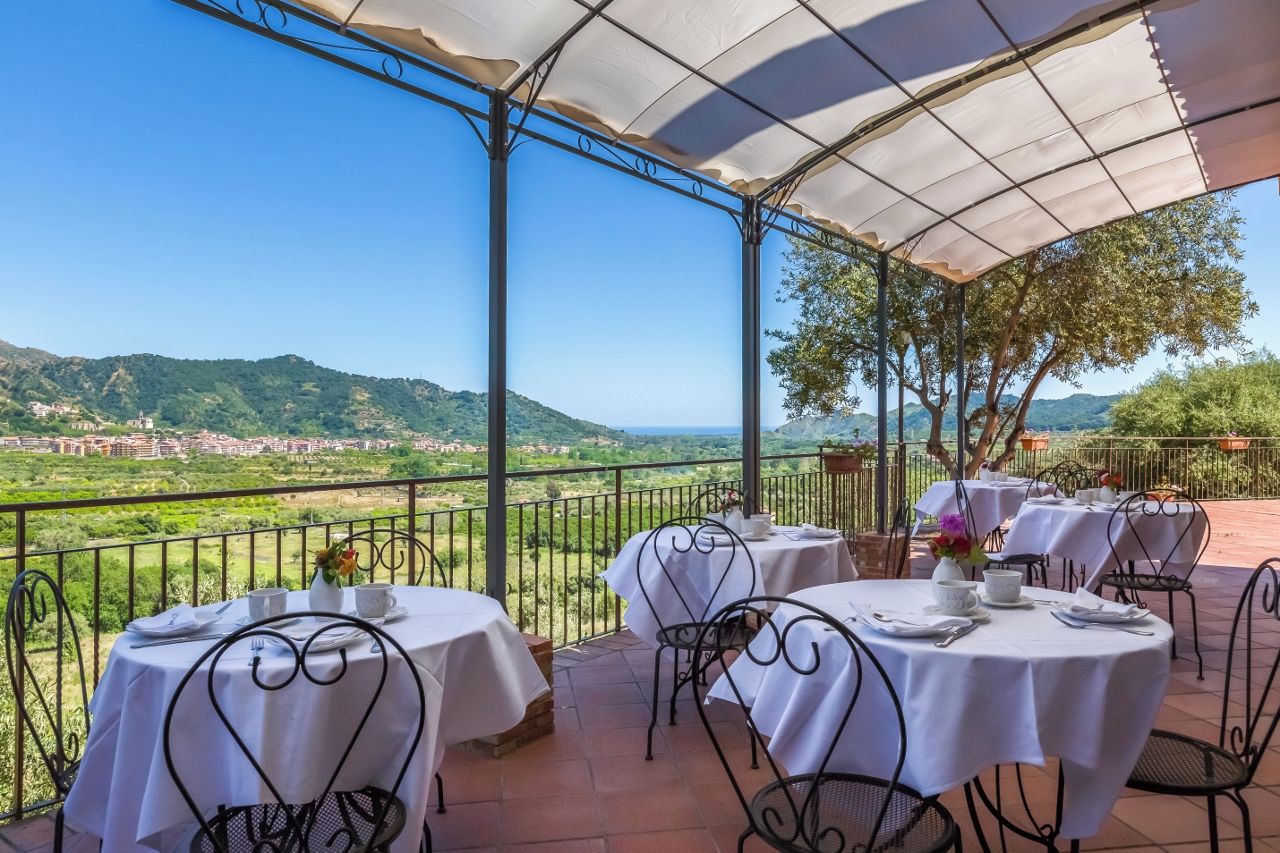 A terrace with tables and chairs, overlooking a scenic landscape with hills and a distant town.