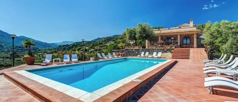 A swimming pool with lounge chairs, a stone wall, and a view of mountains.