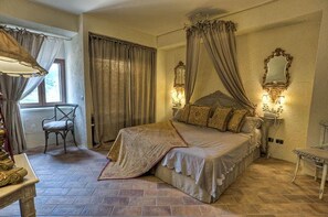 A bedroom with a large bed, a chair, a nightstand with a lamp, and a window with curtains. - Agriturismo Il Poggio Luxury Country Resort (Graniti)