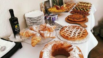 A buffet table with various pastries, a bottle of olive oil, and a stack of plates.