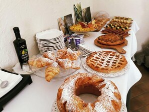 A buffet table with various pastries, a bottle of olive oil, and a stack of plates. - Agriturismo Il Poggio Luxury Country Resort (Graniti)