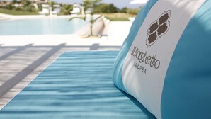A poolside lounge area with a blue-striped towel and a pillow with 'Il Borghetto TROPICA' branding. - Il Borghetto Creative Resort (Tropea)