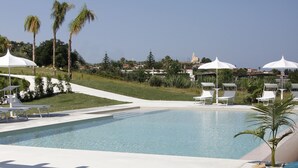 A pool area with lounge chairs and umbrellas, surrounded by palm trees and a clear sky. - Il Borghetto Creative Resort (Tropea)
