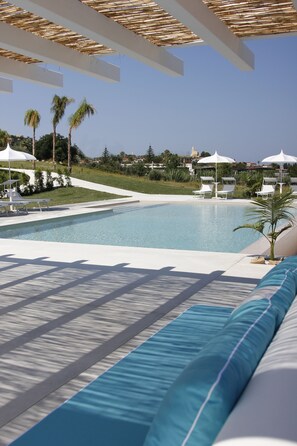 A pool area with lounge chairs and umbrellas, surrounded by palm trees and a clear sky. - Il Borghetto Creative Resort (Tropea)