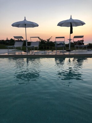 A poolside area with lounge chairs and umbrellas, surrounded by a calm water body reflecting the sky. - Il Borghetto Creative Resort (Tropea)