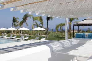 A poolside area with white lounge chairs and umbrellas, a covered seating area, and a view of the ocean. - Il Borghetto Creative Resort (Tropea)