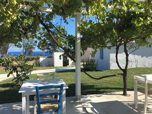 Un espace extérieur aménagé avec des meubles blancs, comprenant une table et des chaises, entouré de verdure et offrant une vue sur la mer.