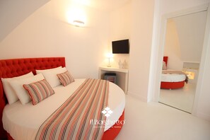 Une chambre à coucher avec une tête de lit rembourrée de tissu rouge, un lit avec une literie à rayures, une table de chevet avec une lampe, un téléviseur à écran plat et un miroir qui reflète la pièce.