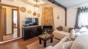 Un salon chaleureux avec une cheminée en pierre, un téléviseur posé sur un meuble sombre et un confortable ensemble de canapés.