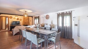 Un vaste espace dédié à la salle à manger, avec une longue table, des chaises en osier et un mur en pierre.