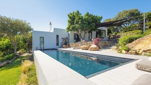 Ein moderner Poolbereich mit klarem Pool, umgeben von einer weißen Liegefläche und naturnaher Bepflanzung.