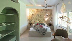 Ein Schlafzimmer mit Steinwand, einem Bett mit Decke, einem Stuhl und einem Regal mit Gegenständen.
