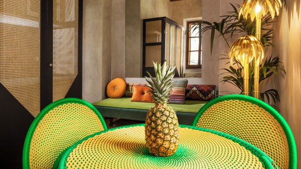 Ein Zimmer mit einem grünen Sofa, einer Ananas als Mittelpunkt und einem Rattan-Tisch.