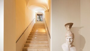 Eine Marmortreppe mit einer Glastür am oberen Ende, die zu einem Raum mit einer ausgestellten Büste führt.