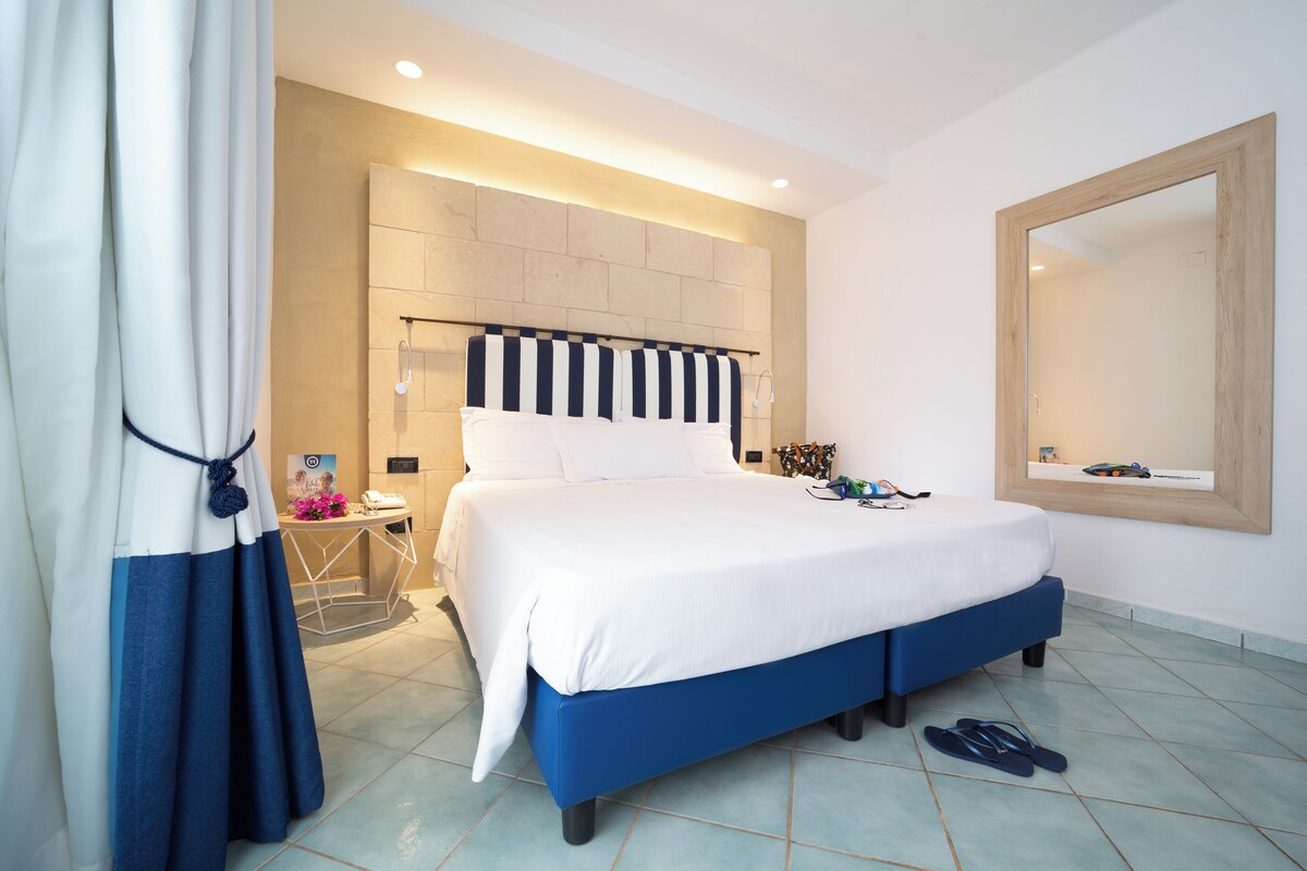 Ein modernes Schlafzimmer mit einem großen Bett, einer Kopfteil mit Streifenmuster, einem Nachttisch mit Lampe und einem großen Spiegel an der Wand.