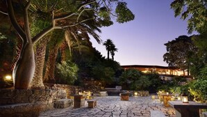 Un patio exterior con pavimento de piedra, zonas de estar y un edificio al fondo.