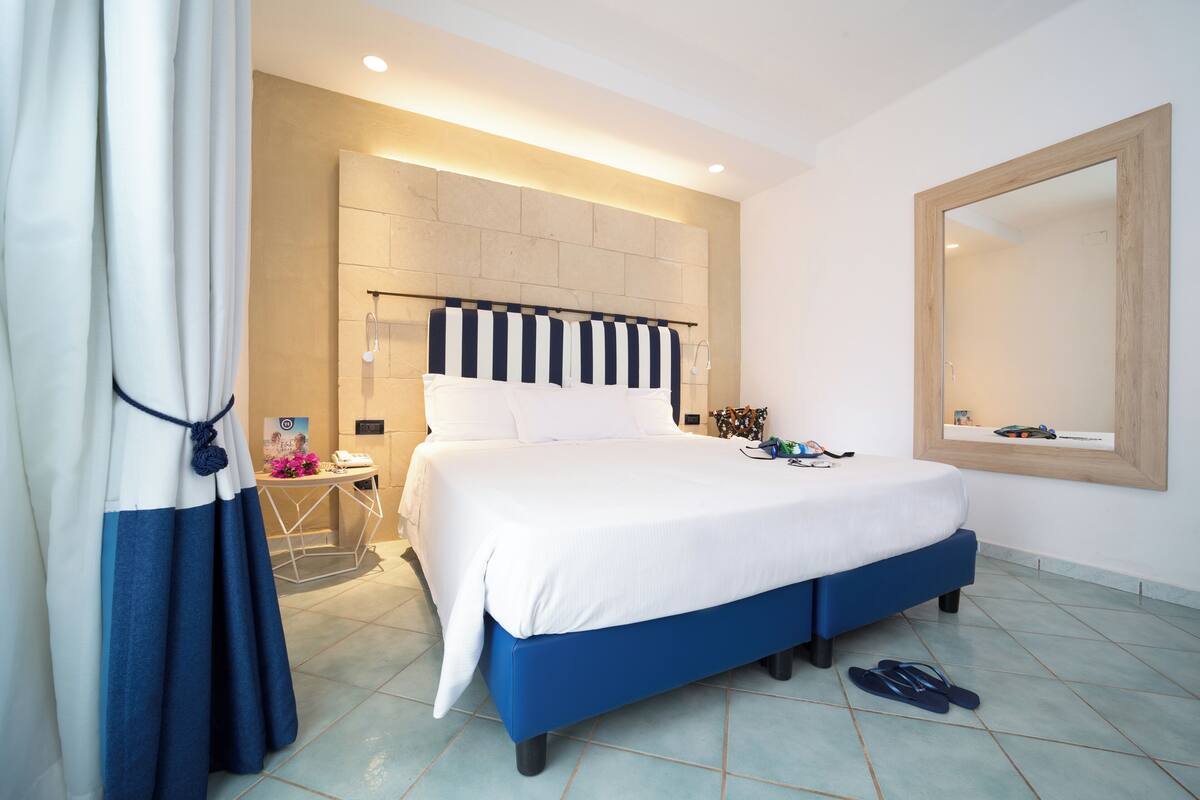 Un dormitorio moderno con una cama grande, cabecera con diseño a rayas, mesita de noche con lámpara y un espejo grande en la pared.