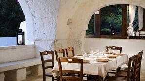 Un área de comedor al aire libre con una mesa blanca para seis personas, sillas de madera y lámparas colgantes.
