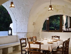 Un espace de restauration en plein air avec une table blanche dressée pour six personnes, des chaises en bois et des lampes suspendues.