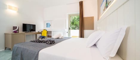 A hotel room with a bed, a desk with a computer, a TV, and a window with curtains.