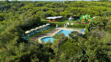 Una vista aerea di un resort con piscina, lettini prendisole e un’area giochi per bambini.
