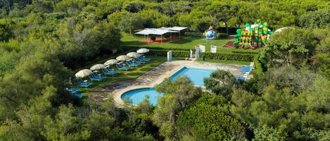 An aerial view of a resort with a swimming pool, sun loungers, and a children's play area.