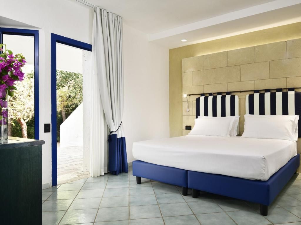 Une chambre moderne avec un grand lit, une vue sur la verdure et un mur d’accent bleu.