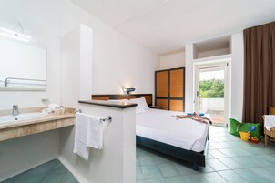 Habitación de hotel con cama, baño con lavabo y espejo, y vista a zonas verdes.