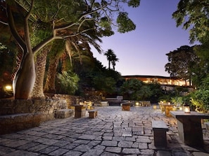 Un patio exterior con pavimento de piedra, zonas de estar y un edificio al fondo.