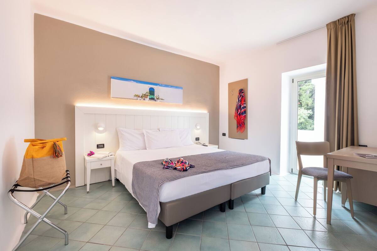 Een hotelkamer met een bed, nachtkastje, stoel en bureau.
