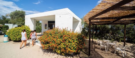 A white building with a covered outdoor seating area and a bush with orange flowers.
