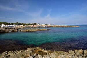 Una playa costera con aguas cristalinas, costas rocosas y sombrillas de playa.