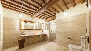 A modern bathroom with a wooden ceiling, a large mirror with lights, a sink, a toilet, and a shower area. - Tenuta Montecucco (Cinigiano)
