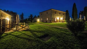 A stone building with a well-lit entrance and a grassy lawn. - Tenuta Montecucco (Cinigiano)