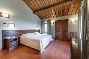 A bedroom with a wooden ceiling, a bed with a headboard, a nightstand, a wardrobe, and two wall-mounted lights. - Tenuta Montecucco (Cinigiano)